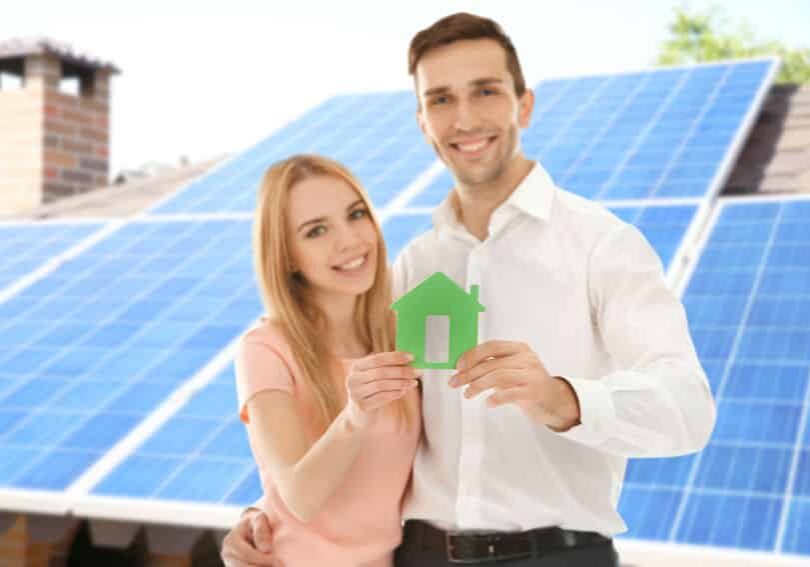 Young couple holding figure of house and solar panels on background